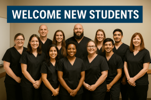 A group of massage students all wearing black scrubs standing together under a banner that says Welcome New Students