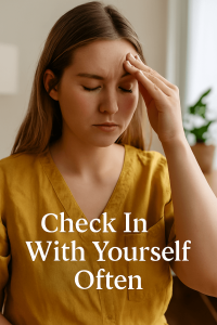 A young woman in a mustard-yellow shirt gently touches her forehead with eyes closed, appearing tired or pensive. Soft daylight filters through the room, and white overlay text reads “Check In With Yourself Often.”